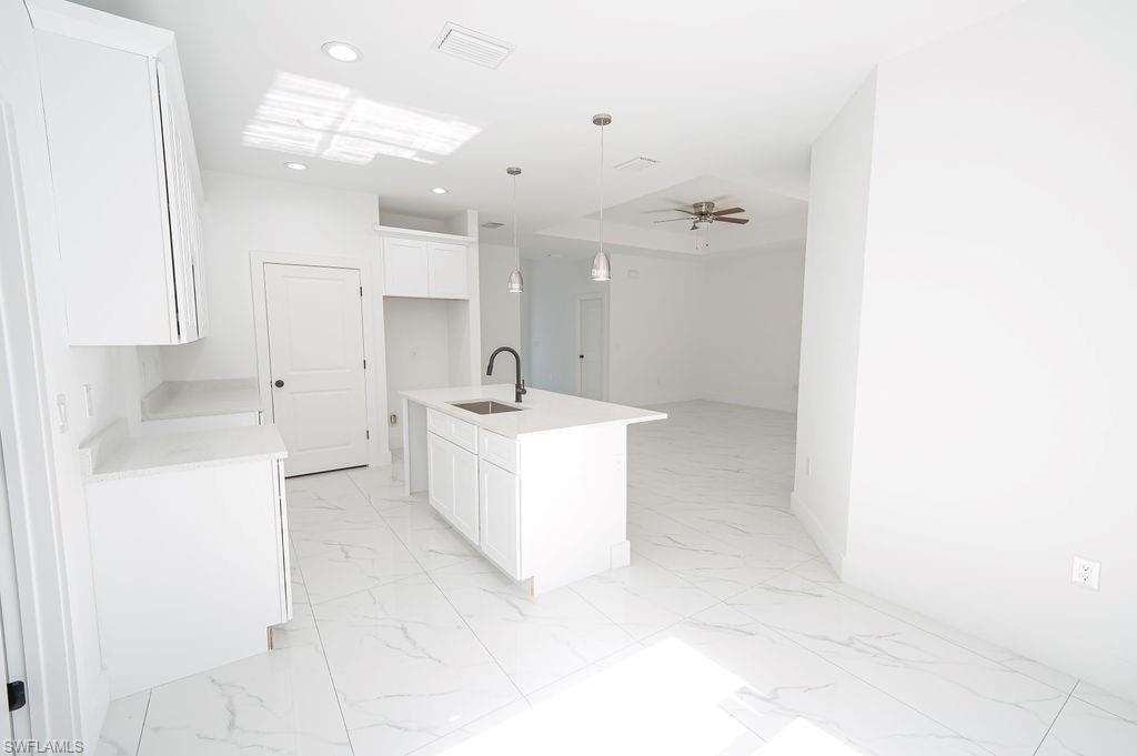 Kitchen featuring decorative light fixtures, white cabinets, a center island with sink, light marble finish flooring, and recessed lighting.Photos are of a staged model or similar plan. Features and finishes may vary.