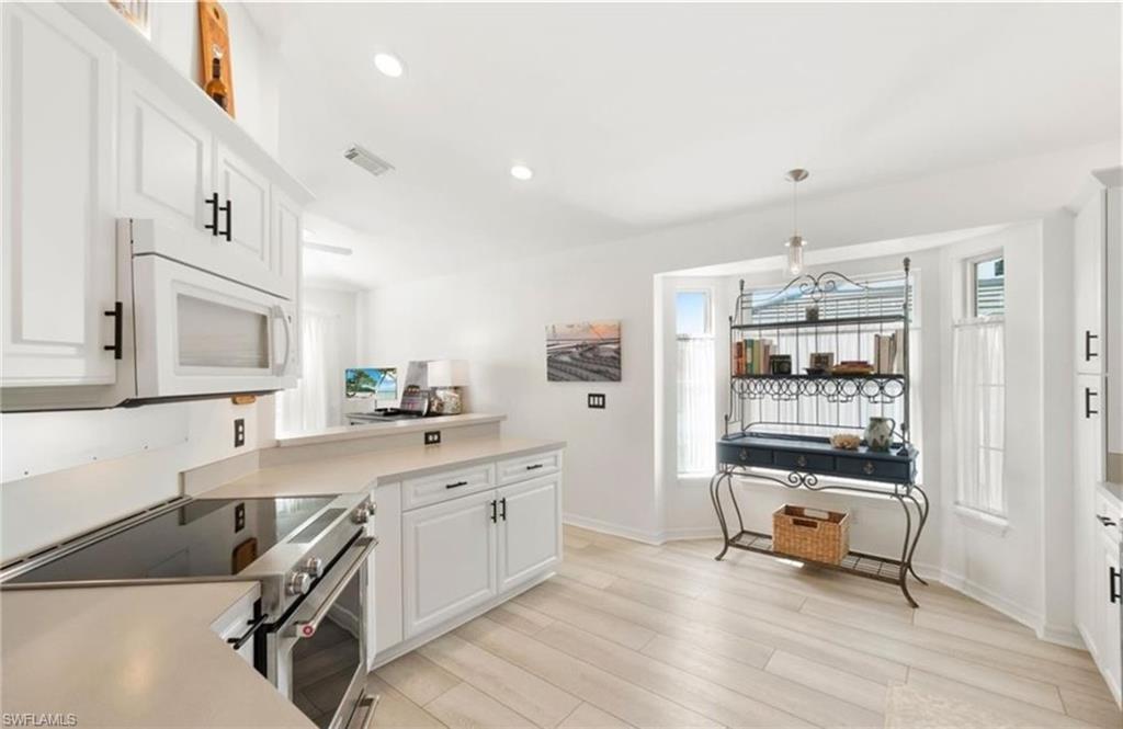 Kitchen with visible vents, light wood finished floors, white cabinetry, white microwave, and stainless steel electric stove
