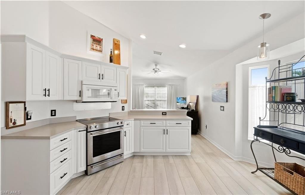 Kitchen featuring light countertops, a peninsula, white cabinets, white microwave, and stainless steel electric range oven