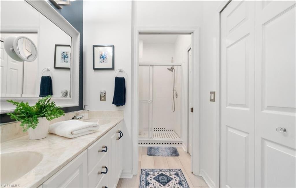 Bathroom with a stall shower, double vanity, wood finished floors, and a sink