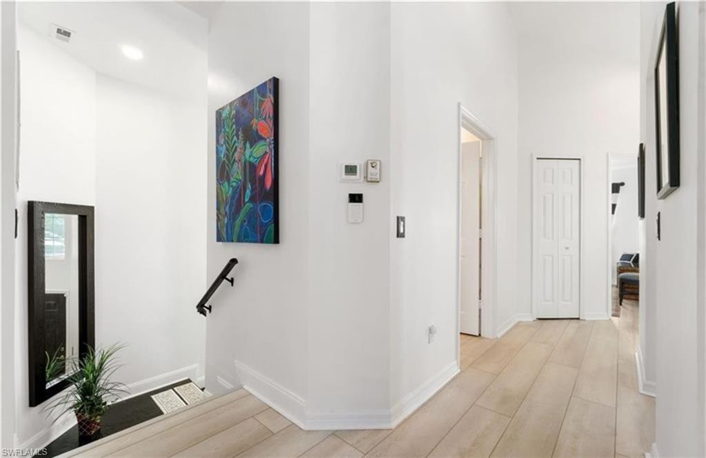 Hallway featuring baseboards, light wood-type flooring, visible vents, and a towering ceiling