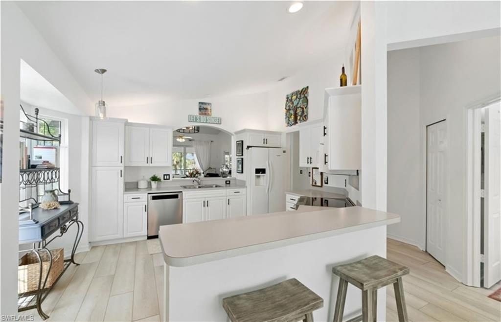 Kitchen with white fridge with ice dispenser, a sink, vaulted ceiling, and stainless steel dishwasher