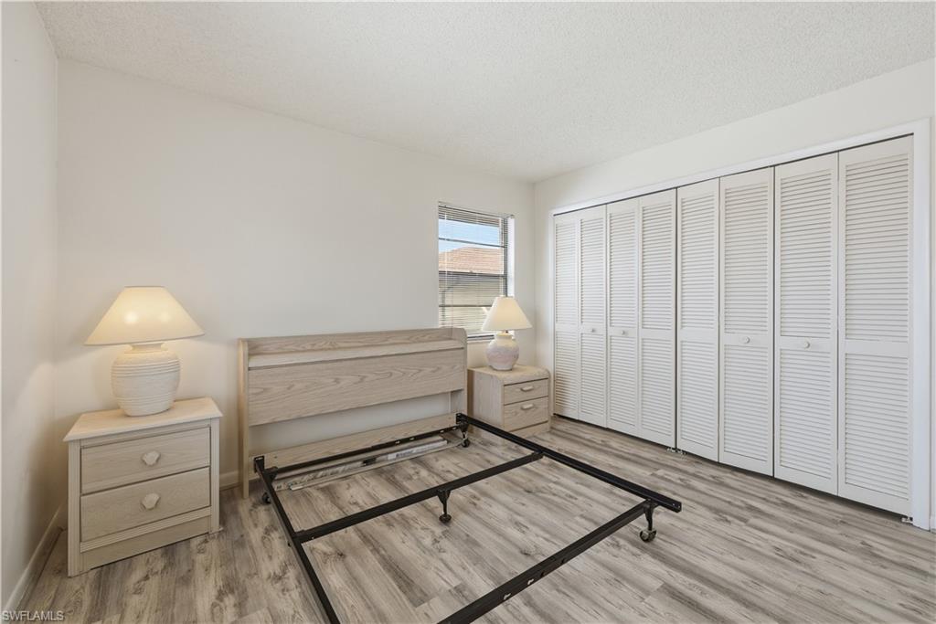 Wood-finish flooring with white louvered closet doors, a single window, and textured white walls