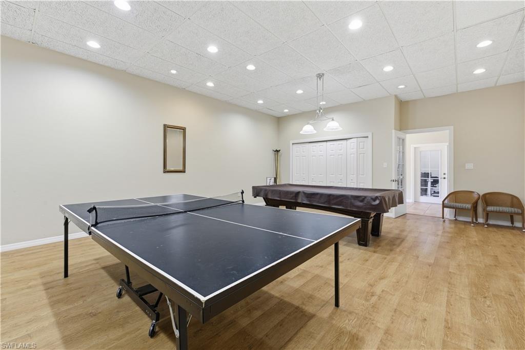 Spacious recreational room featuring wood-finish flooring, a drop ceiling with recessed lighting, and a pendant light fixture