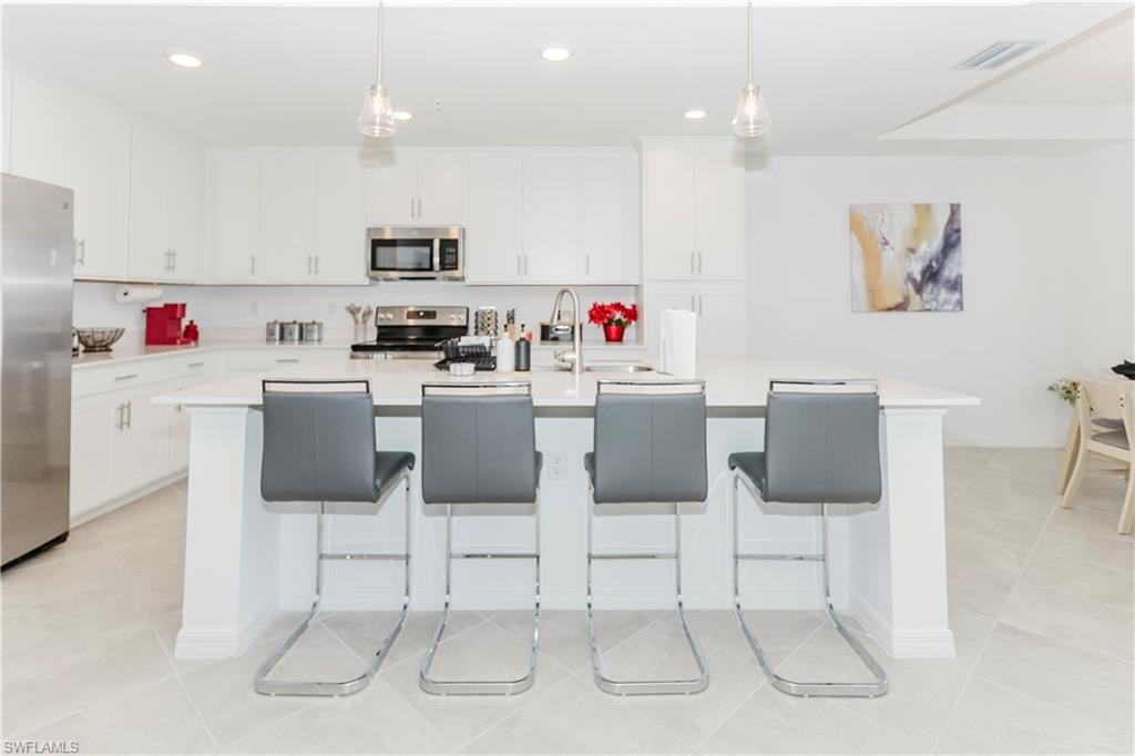 Kitchen with stainless steel appliances, light tile patterned flooring, an island with sink, light countertops, and white cabinets