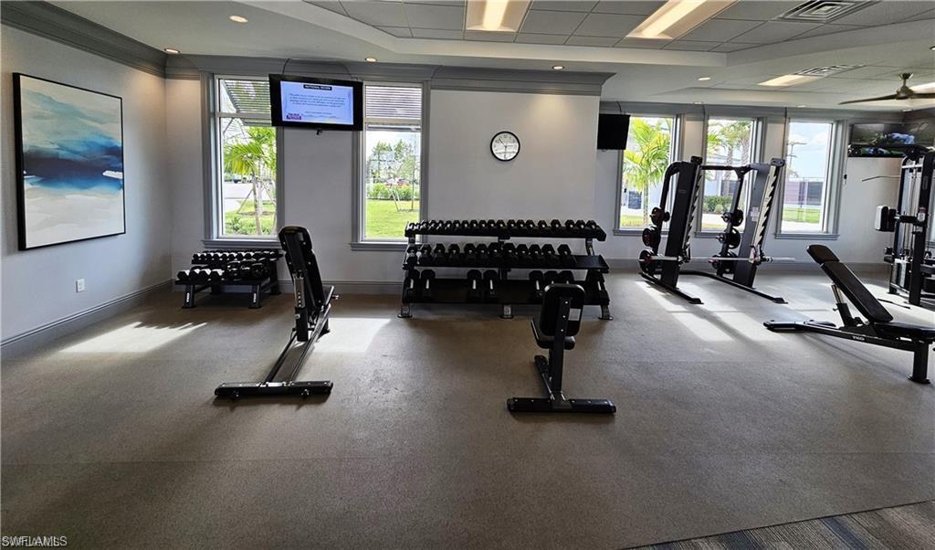 Gym with baseboards, visible vents, a drop ceiling, and a healthy amount of sunlight