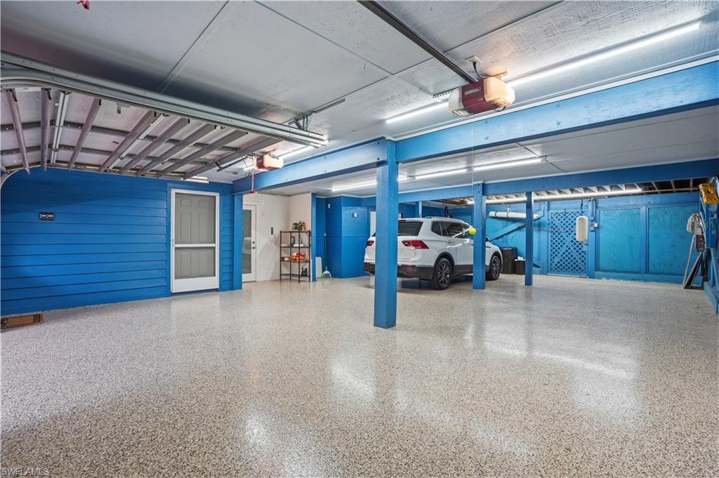 Spacious garage featuring a durable epoxy floor, exposed beam ceiling, bright overhead lighting, and dedicated access door