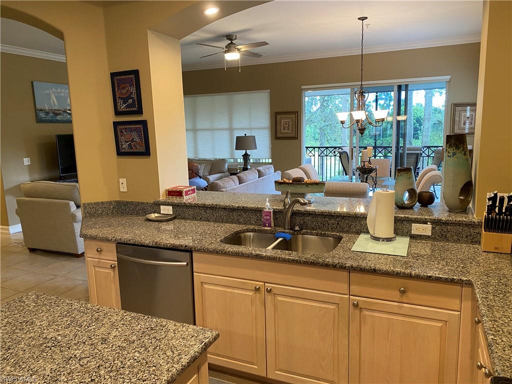 Kitchen featuring open floor plan, crown molding, dark stone countertops, hanging lights, and a ceiling fan
