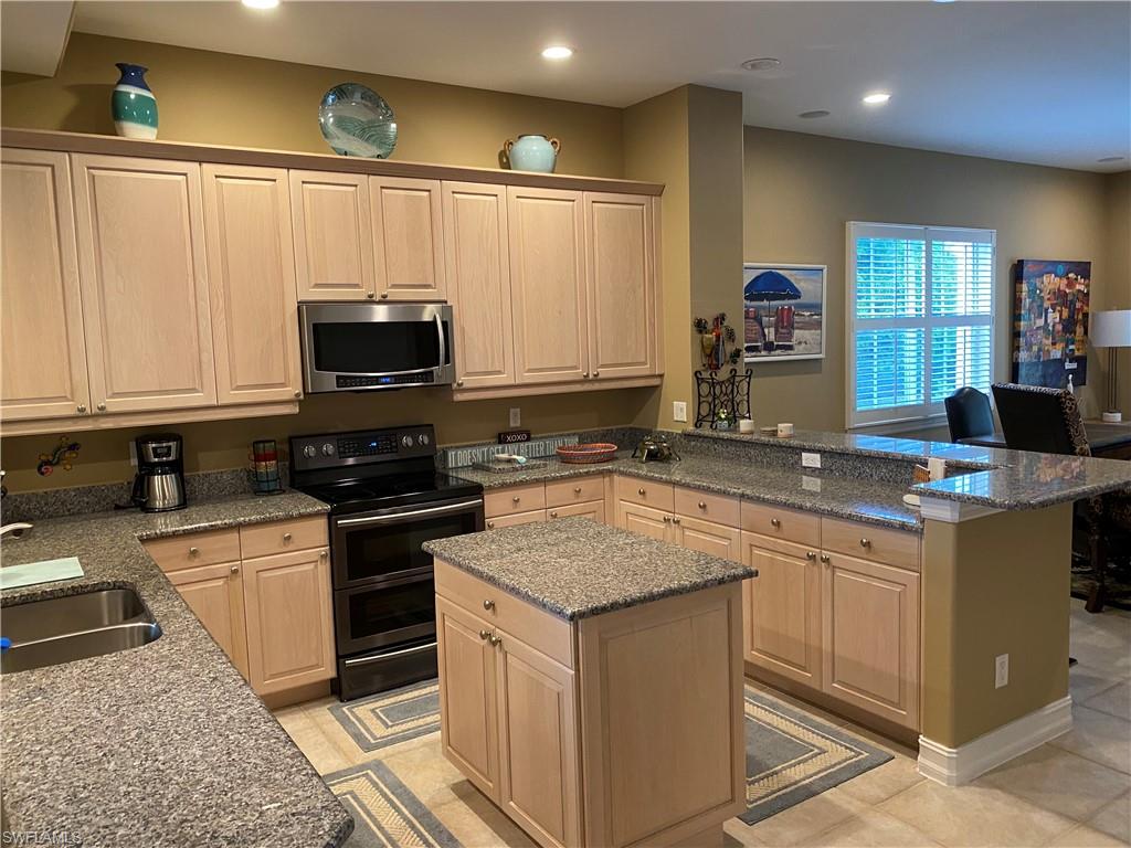 Kitchen with range with two ovens, light wood finish cabinets, stainless steel microwave, a center island, and dark stone counters