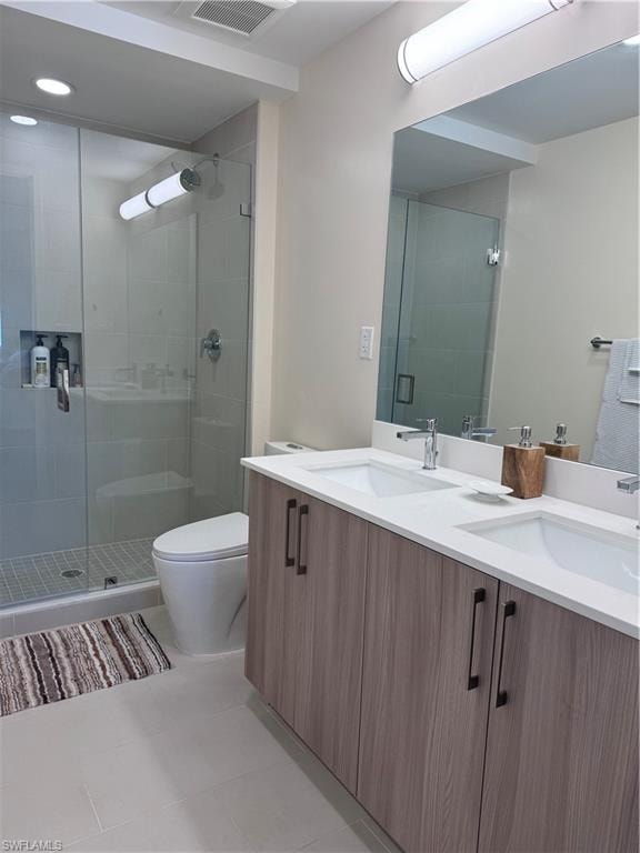Bathroom with an enclosed shower, vanity, tile patterned floors, and toilet