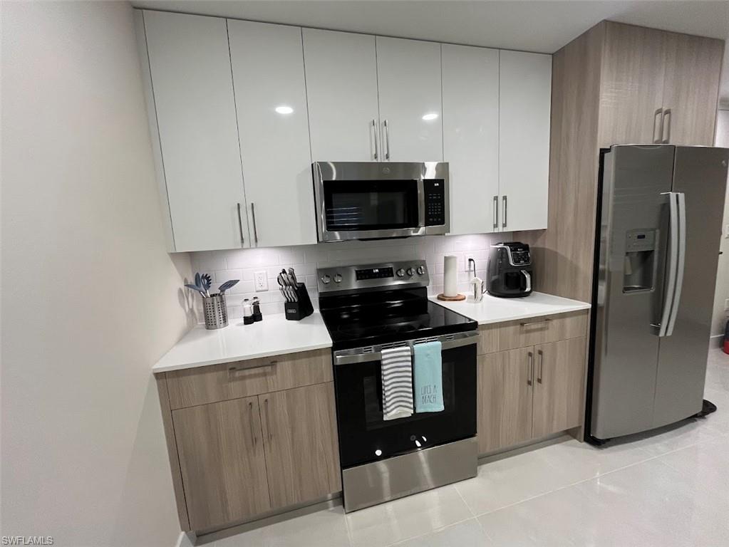 Kitchen with stainless steel appliances, backsplash, modern cabinets, and light tile patterned flooring