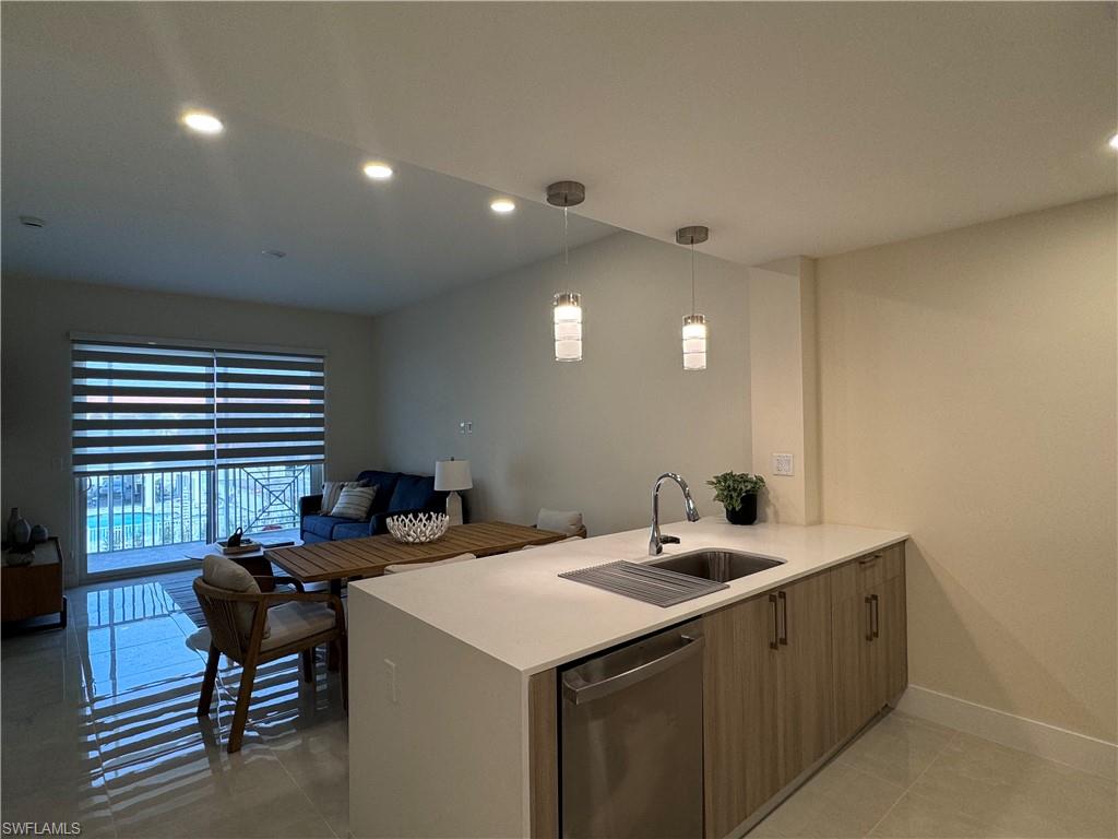 Kitchen with tile patterned floors, kitchen peninsula, hanging light fixtures, sink, and stainless steel dishwasher