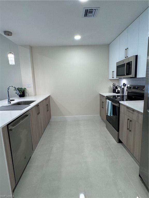 Kitchen with sink, dishwashing machine, white cabinets, stove, and pendant lighting