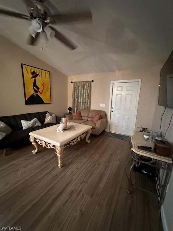 Living room with ceiling fan, vaulted ceiling, and dark wood-type flooring