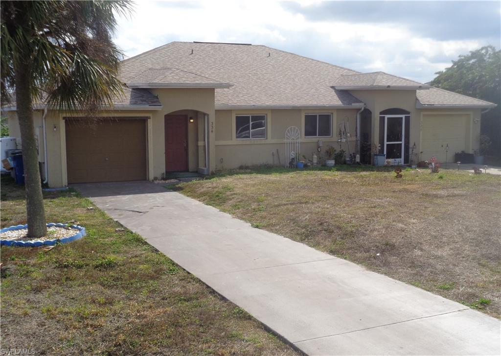 Left view of front of the duplex with a garage for each unit, roof with shingles, stucco siding, a front yard, and concrete driveway