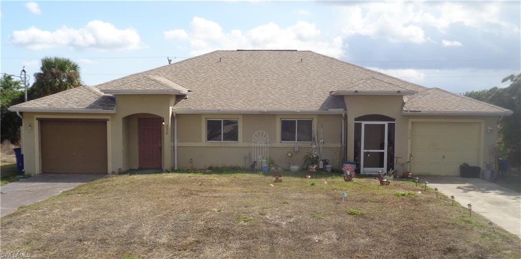 Traditional duplex featuring stucco siding, roof with shingles, a garage, concrete driveway, and a front lawn