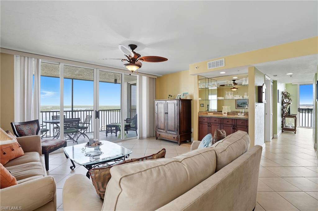 Living room with a wall of windows, light tile patterned flooring, a ceiling fan, and a water view - Virtually Edited Image