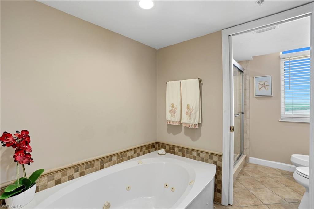 Full bathroom featuring a whirlpool tub, light tile patterned floors, and a stall shower - Virtually Edited Image