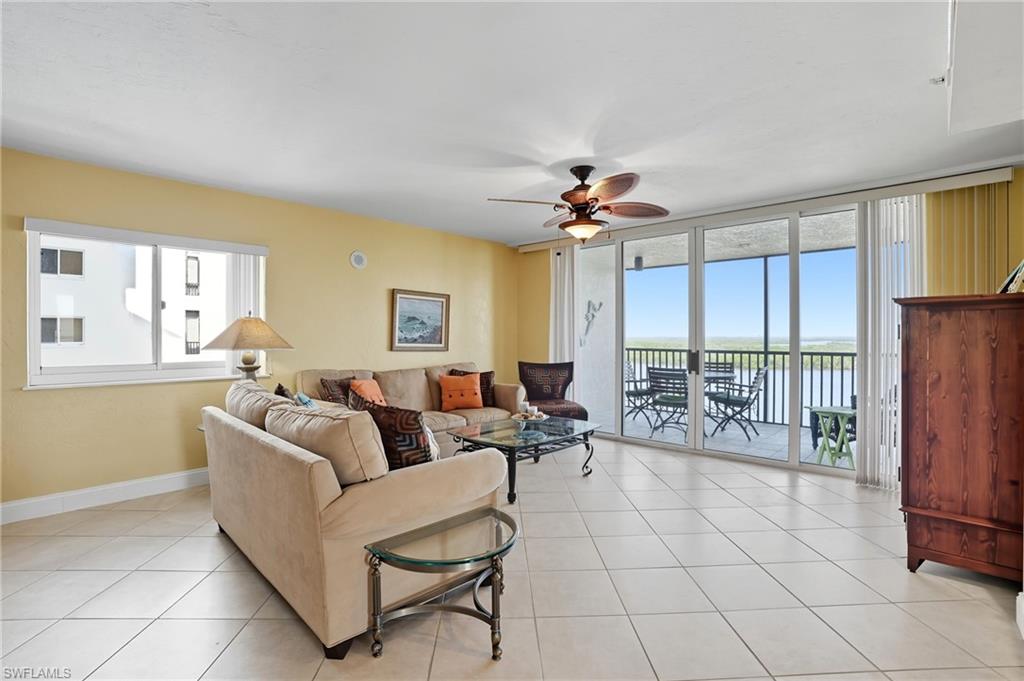 Living room featuring healthy amount of natural light, light tile patterned floors, a ceiling fan, a water view, and floor to ceiling windows - Virtually Edited Image