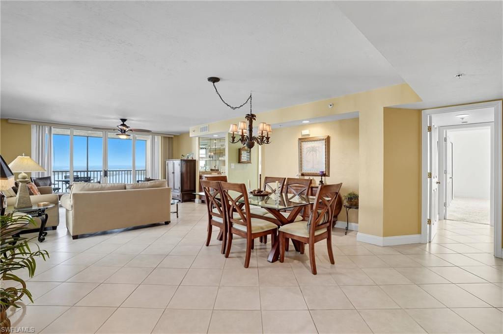 Dining space featuring light tile patterned floors, a chandelier, a ceiling fan, expansive windows, and a water view - Virtually Edited Image