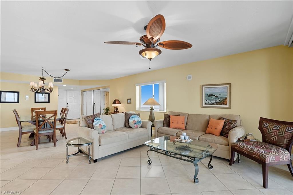 Living area with light tile patterned flooring, ceiling fan, and a chandelier - Virtually Edited Image