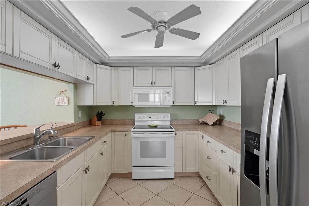 Kitchen with appliances with stainless steel finishes, white cabinetry, light tile patterned flooring, light countertops, and crown molding - Virtually Edited Image