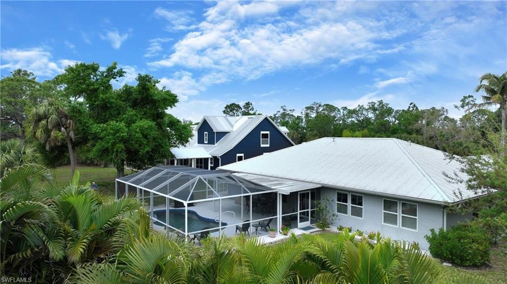 Rear view of property with an outdoor pool, glass enclosure, a sunroom, and a metal roof