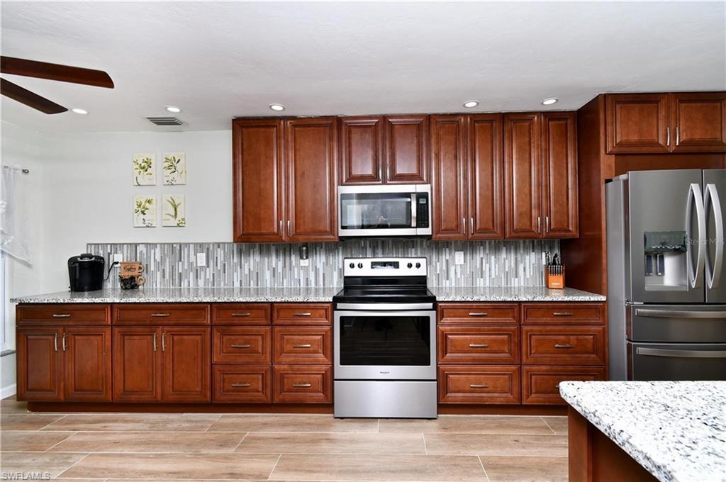 Kitchen featuring stainless steel appliances, light stone countertops, wood finish floors, a ceiling fan, and backsplash
