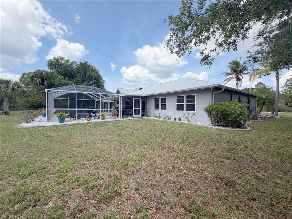 Rear view of property featuring a lanai, a lawn, a sunroom, a patio area, and stucco siding