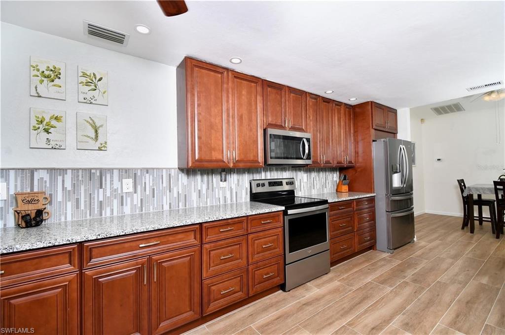Kitchen with stainless steel appliances, ceiling fan, light stone countertops, wood finish cabinetry, and recessed lighting