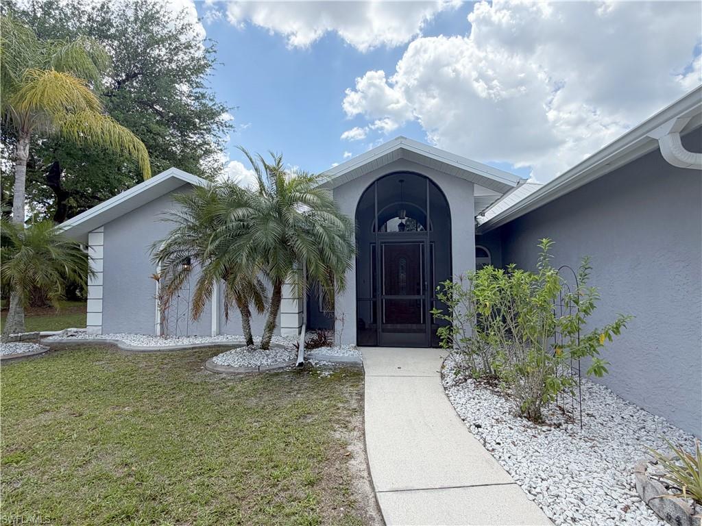 View of exterior entry with stucco siding and a lawn
