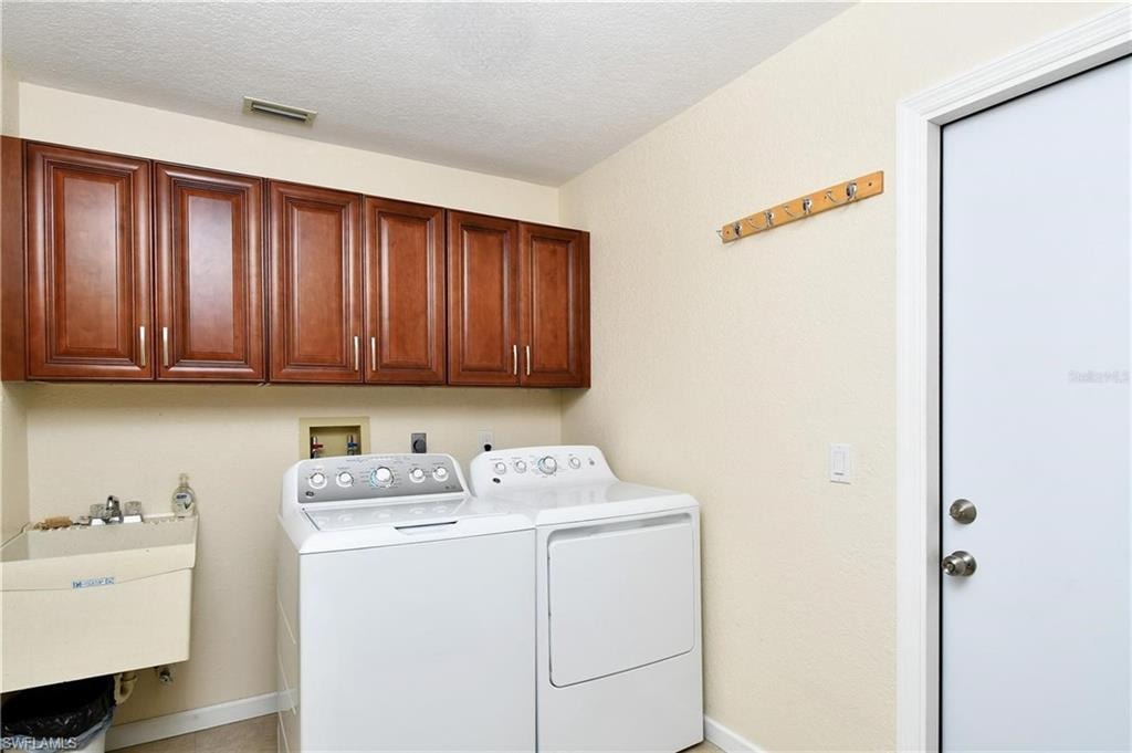 Laundry area with washing machine and clothes dryer, cabinet space, and a textured ceiling