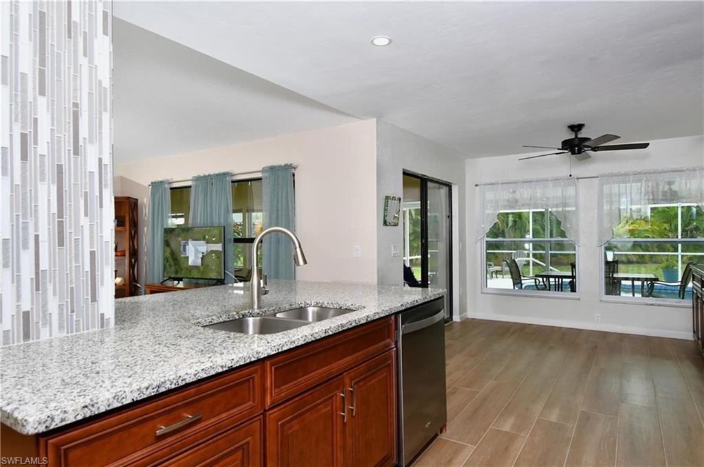 Kitchen featuring a ceiling fan, stainless steel dishwasher, light wood-style floors, light stone counters, and plenty of natural light