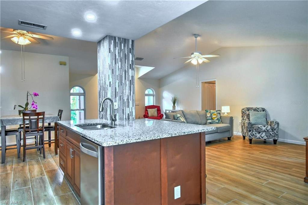 Kitchen featuring ceiling fan, open floor plan, wood finish floors, light stone counters, and wood finish cabinets