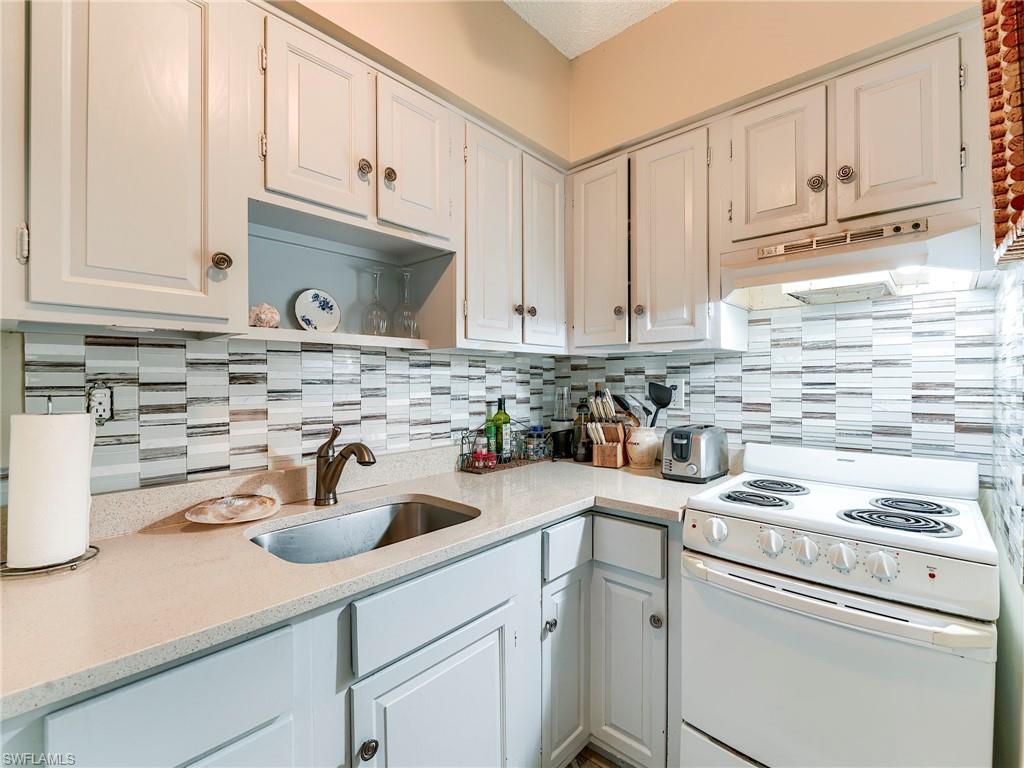 Kitchen with electric range, light stone counters, white cabinets, and tasteful backsplash