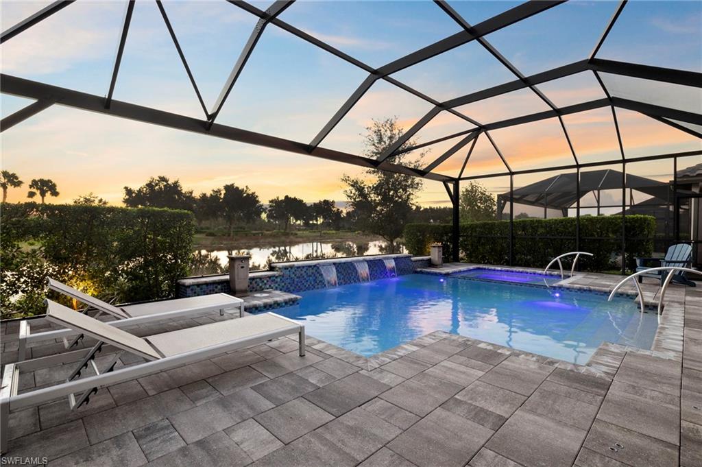 Pool at dusk featuring a jacuzzi, a patio area, pool water feature, a water view, and a lanai