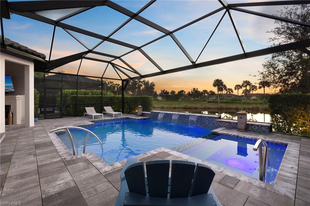 Pool at dusk featuring a water view, an in ground hot tub, a lanai, a patio area, and pool water feature