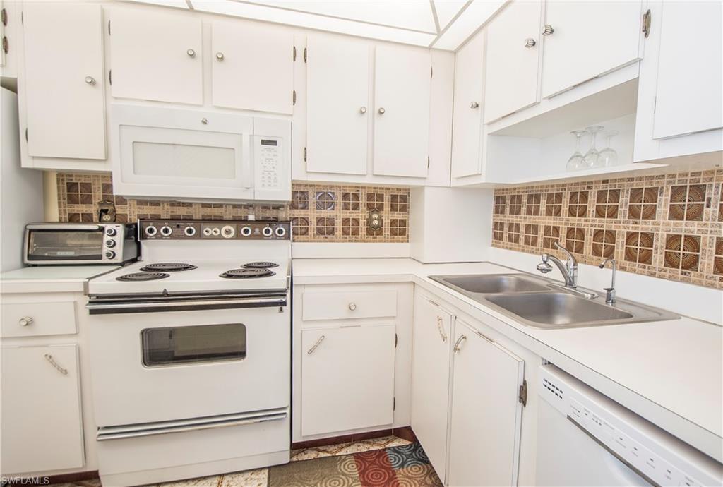 Kitchen with white appliances, light countertops, white cabinets, tasteful backsplash, and open shelves