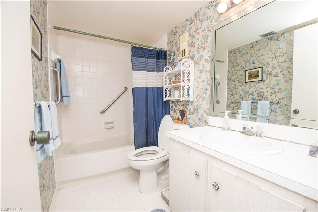 Bathroom featuring wallpapered walls, vanity, and shower / tub combo