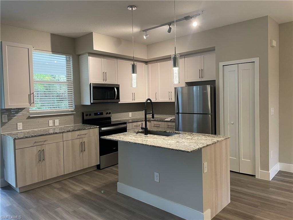 Kitchen with stainless steel appliances, light stone countertops, dark wood-style flooring, a center island with sink, and hanging light fixtures