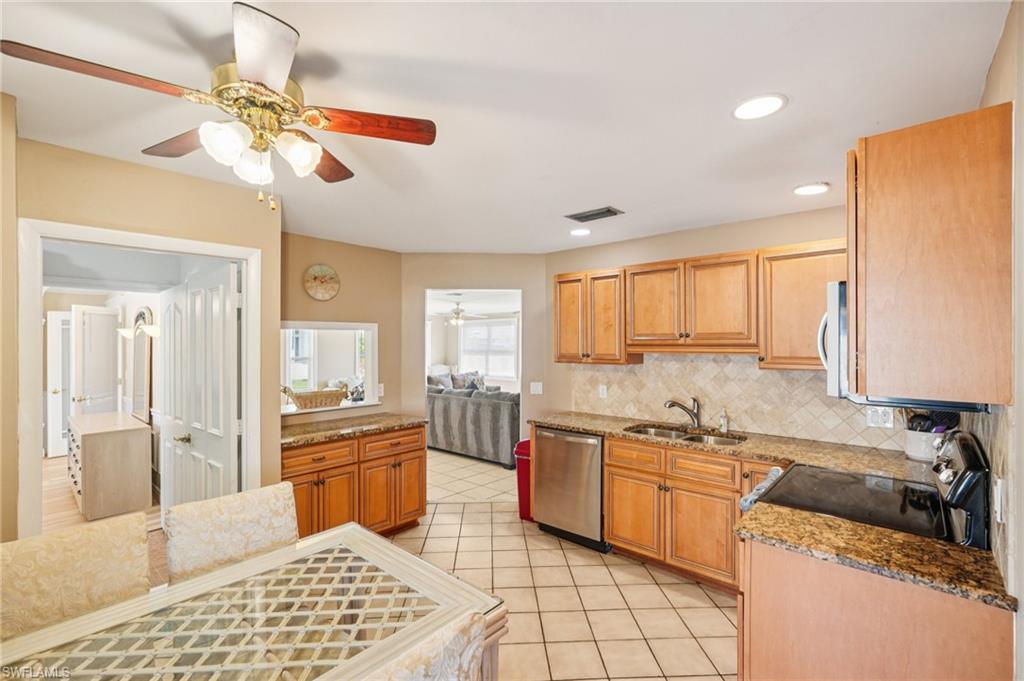 Kitchen featuring a ceiling fan, stainless steel appliances, light stone counters, light tile patterned flooring, and backsplash