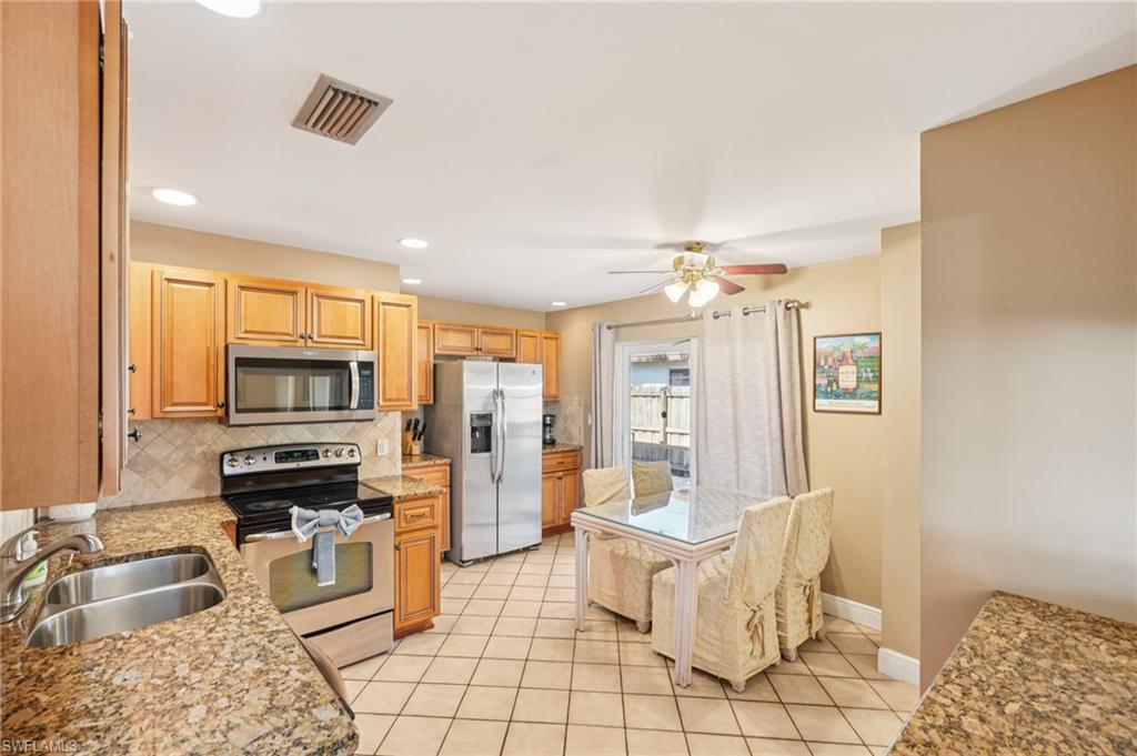 Kitchen featuring stainless steel appliances, a ceiling fan, light stone counters, light tile patterned flooring, and recessed lighting