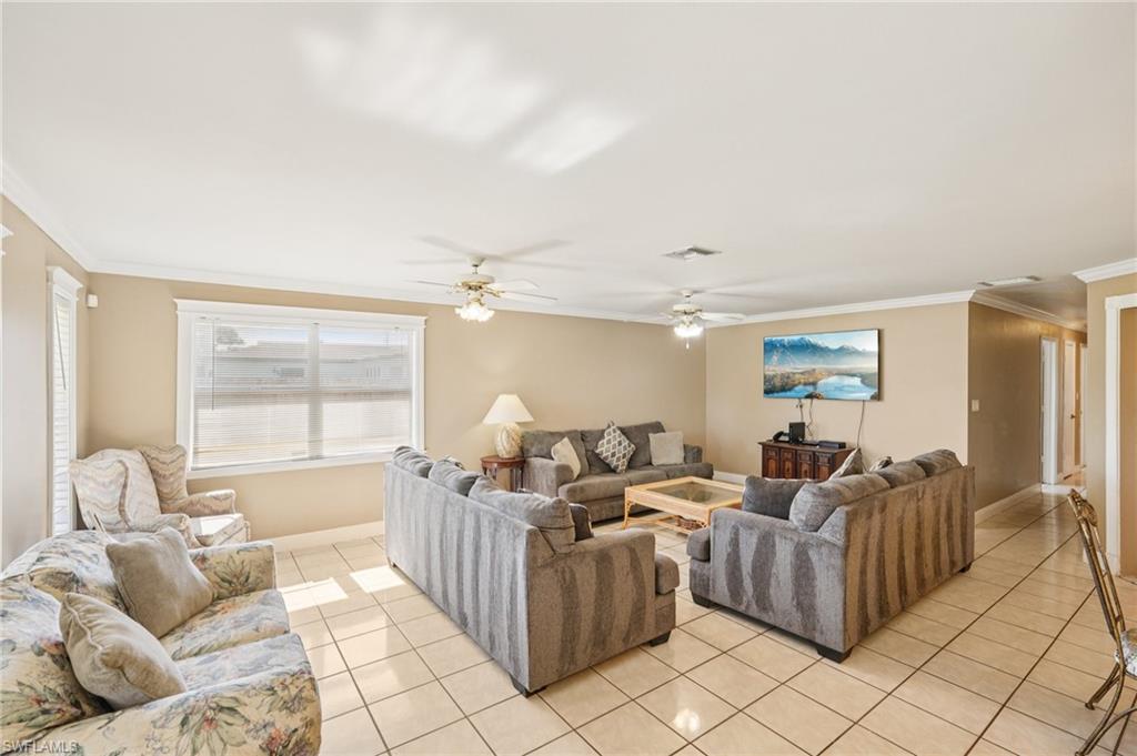 Living room with crown molding, light tile patterned floors, and a ceiling fan