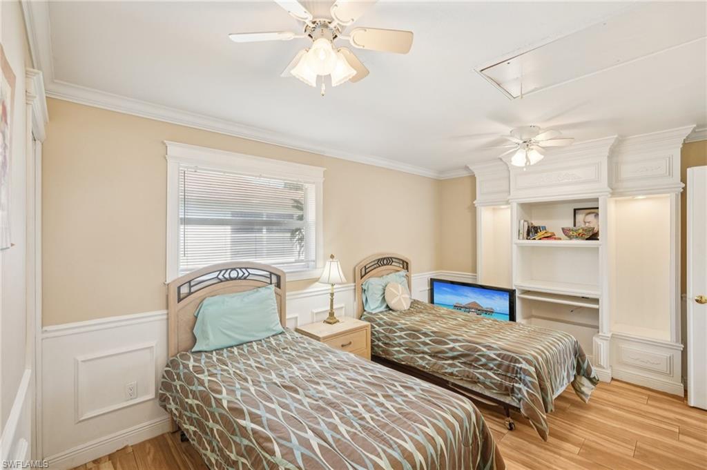 Bedroom with ornamental molding, light wood finished floors, a ceiling fan, a decorative wall, and wainscoting