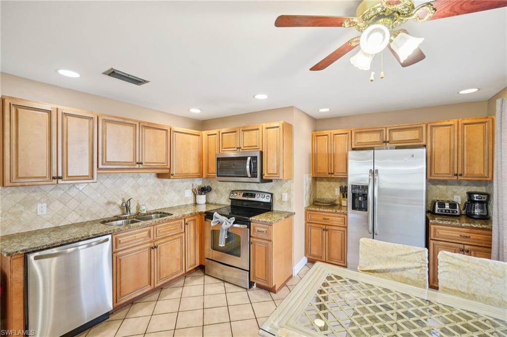Kitchen featuring stainless steel appliances, dark stone counters, light tile patterned floors, a ceiling fan, and recessed lighting