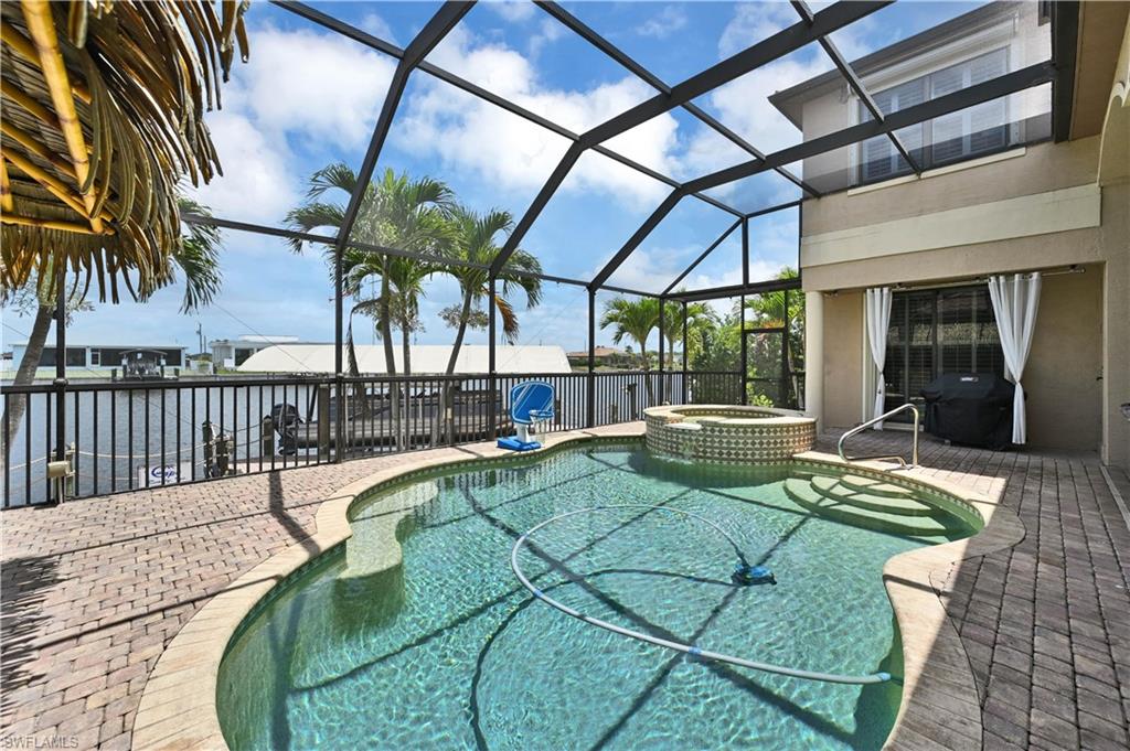 Screened outdoor living area featuring a free-form swimming pool with integrated spa, paver patio, and canal frontage