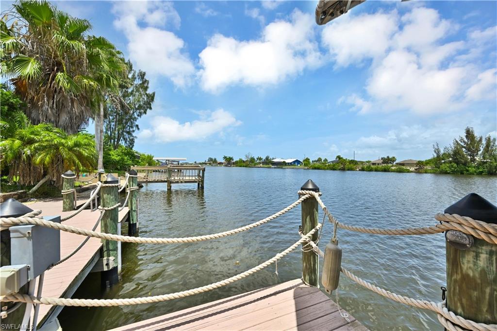 Waterfront property featuring a wood-finish dock with nautical rope railings, multiple palm trees, and canal access