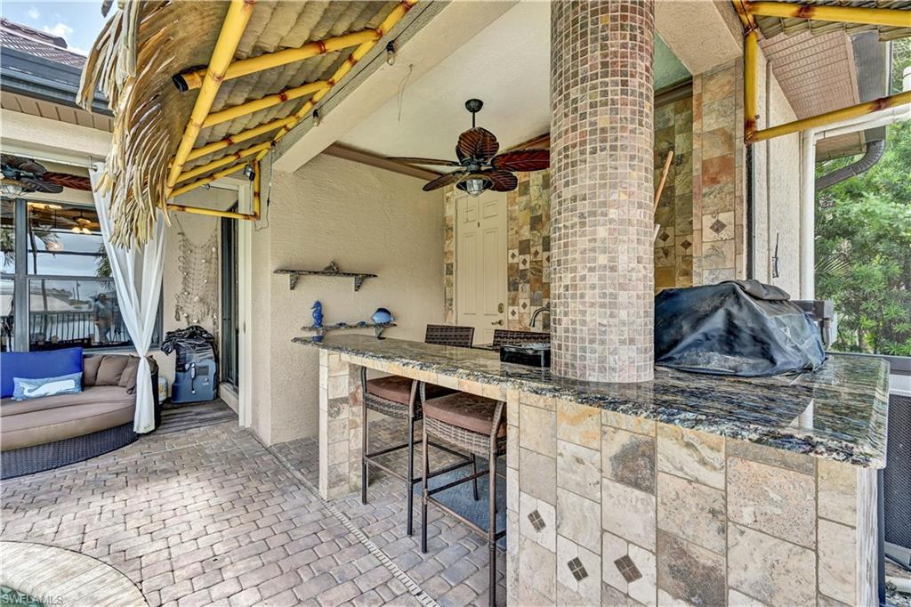 Outdoor kitchen bar with a granite countertop, tile base, integrated sink, and ceiling fan
