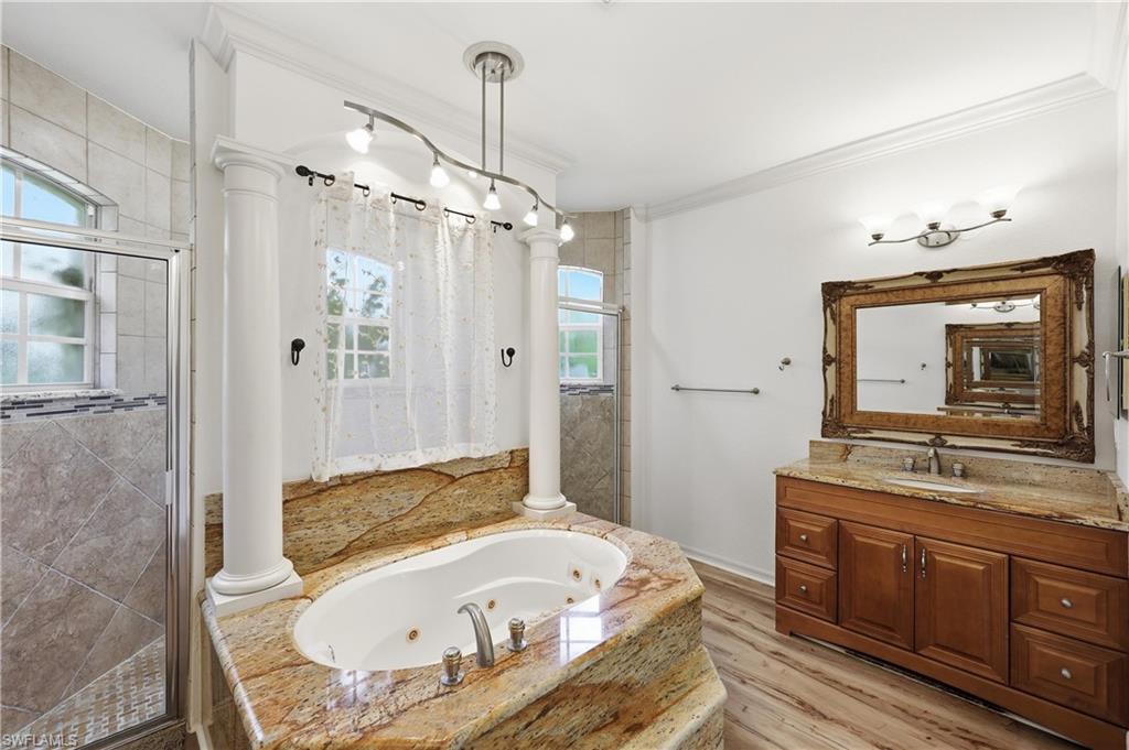 Primary bathroom featuring a soaking tub, granite surround, dual-sink vanity, and separate glass-enclosed shower.
