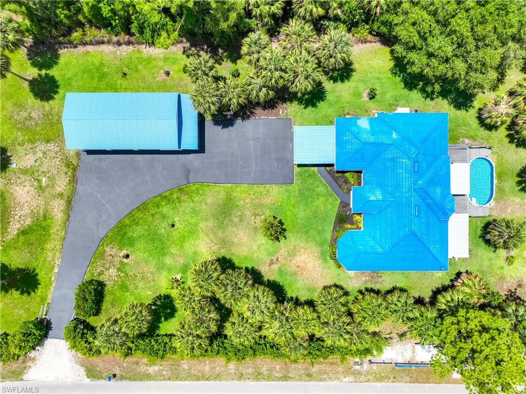Bird's-eye view showcases the circular driveway, detached steel garage, pool deck, and landscaped front yard.